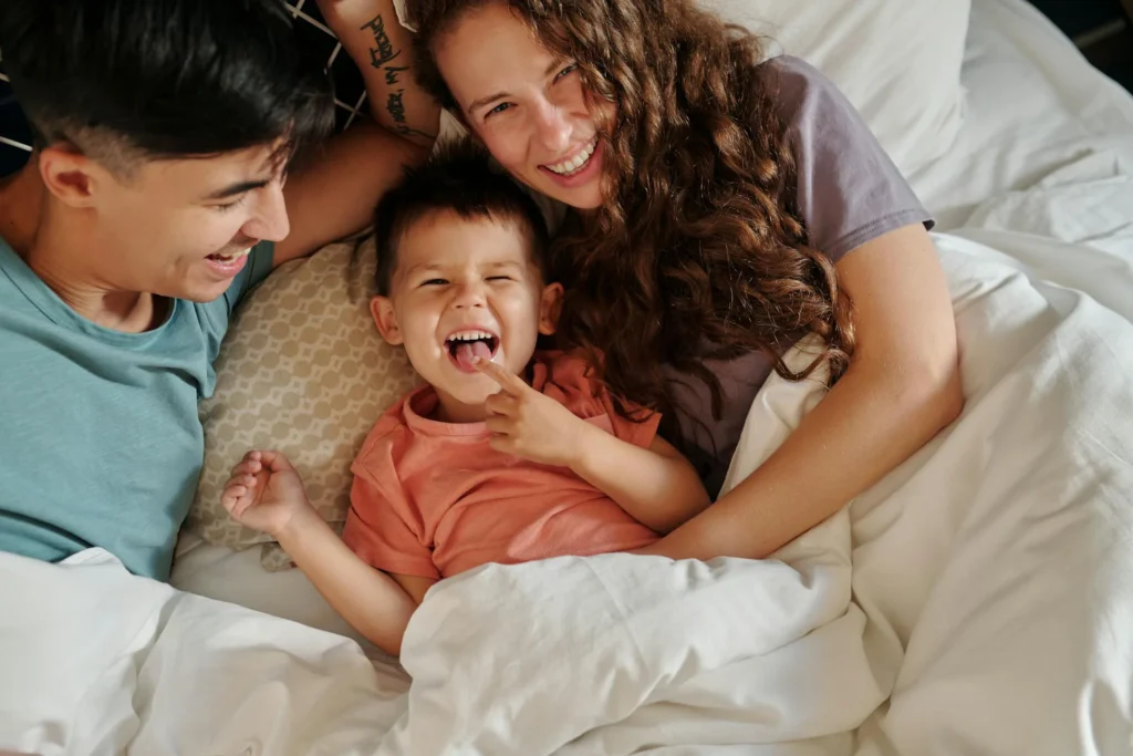 Nell'immagine un uomo, una donna e un bambino sorridono sdraiati su un letto.