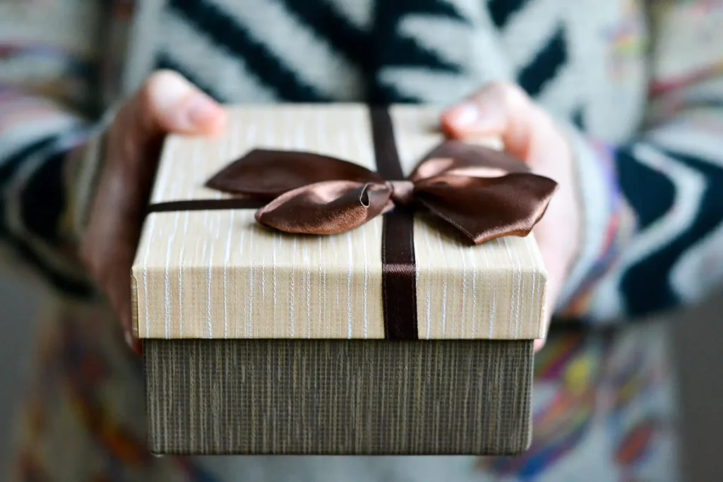 In the picture a person is donating a brown gift. The present has a big brown ribbon on it.